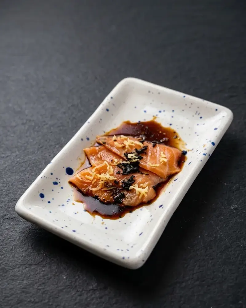Fatias de salmão com molho ponzu em travessa branca pontilhada de azul